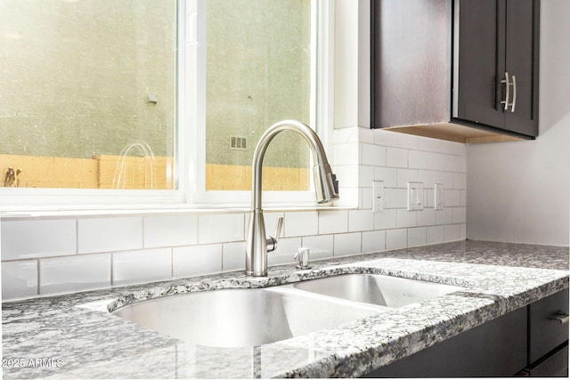 details with dark brown cabinetry, light stone counters, backsplash, and a sink