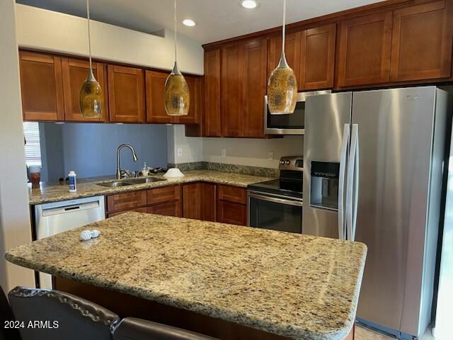 kitchen featuring a kitchen bar, appliances with stainless steel finishes, hanging light fixtures, light stone counters, and sink