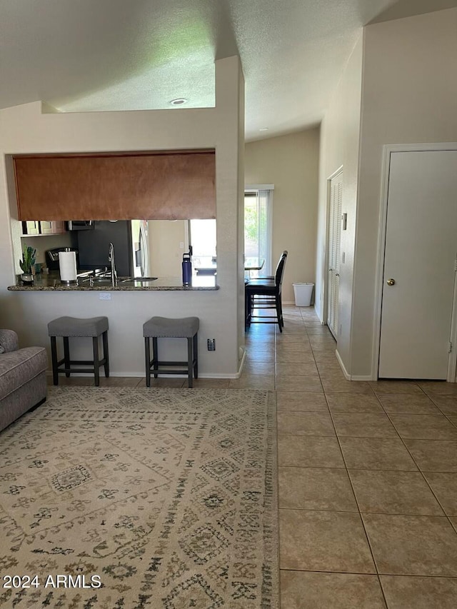 kitchen featuring kitchen peninsula, a kitchen breakfast bar, tile patterned flooring, vaulted ceiling, and sink