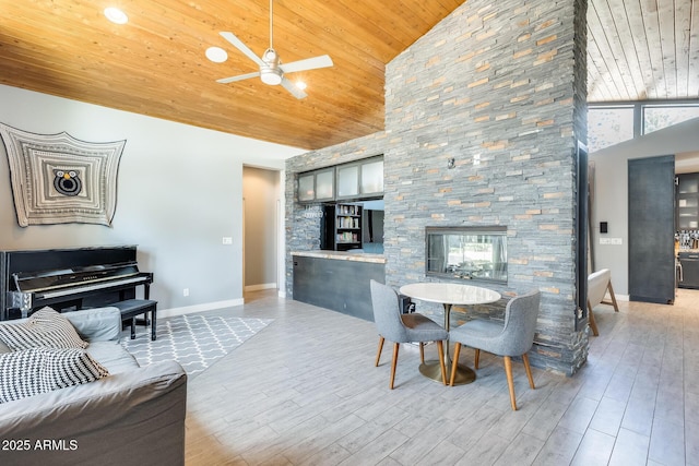 dining area featuring a stone fireplace, wooden ceiling, ceiling fan, and high vaulted ceiling