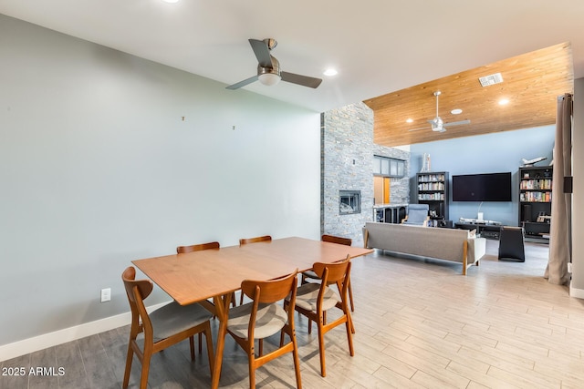 dining area featuring a ceiling fan, baseboards, light wood-style flooring, and a fireplace