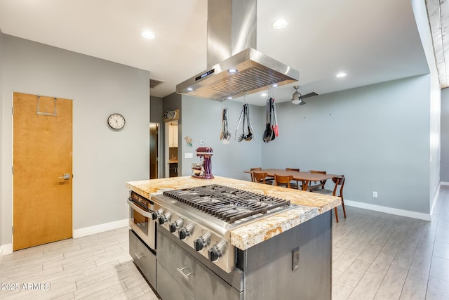 kitchen with island exhaust hood, light countertops, baseboards, stainless steel appliances, and light wood-style flooring