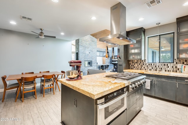 kitchen with ceiling fan, backsplash, island range hood, visible vents, and appliances with stainless steel finishes