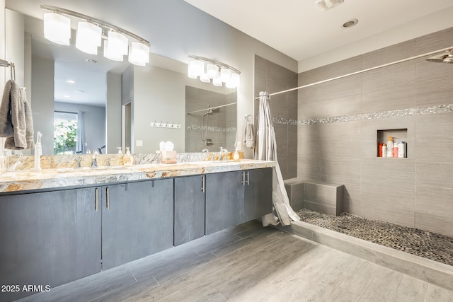 bathroom featuring double vanity, a shower stall, wood finished floors, and a sink
