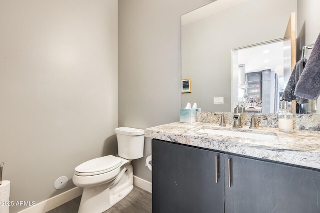 half bathroom with baseboards, vanity, toilet, and wood finished floors