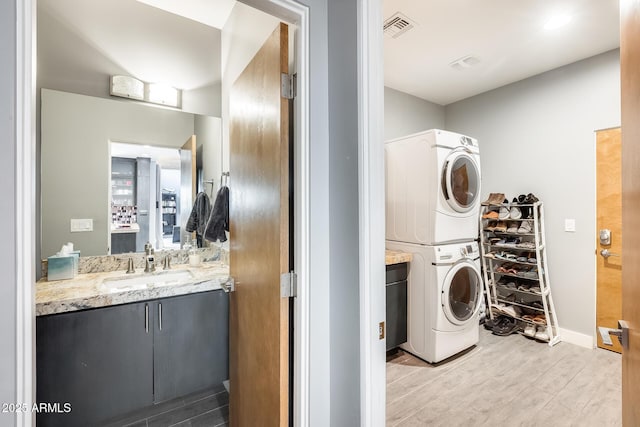 laundry area with visible vents, stacked washer and dryer, laundry area, light wood-type flooring, and a sink