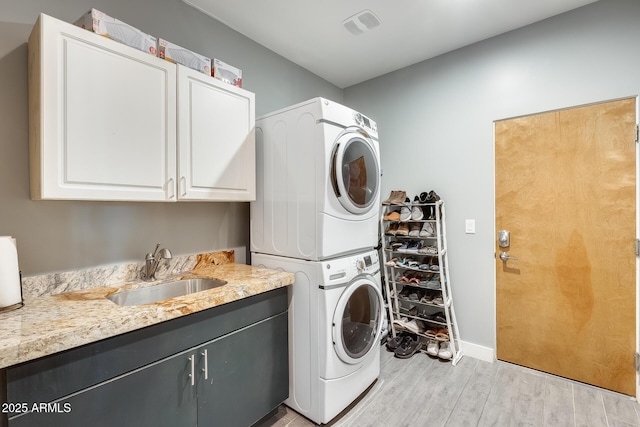 washroom with stacked washer / dryer, visible vents, cabinet space, a sink, and light wood-style flooring