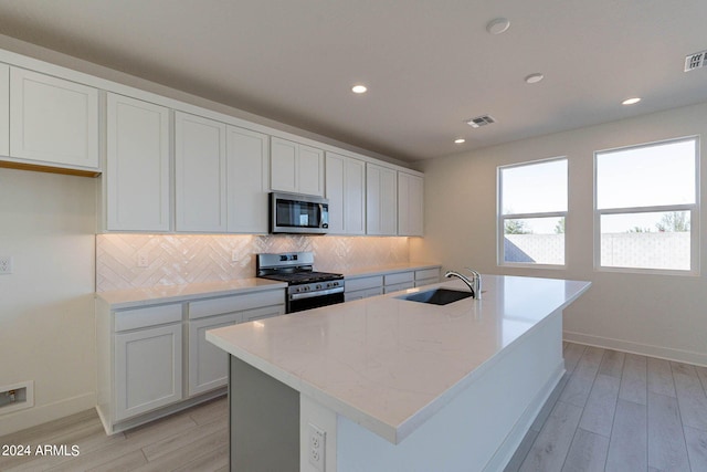 kitchen featuring a center island with sink, appliances with stainless steel finishes, white cabinetry, light hardwood / wood-style floors, and sink