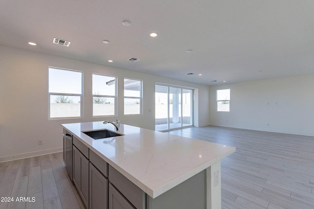 kitchen with dishwasher, a kitchen island with sink, light hardwood / wood-style flooring, sink, and light stone countertops