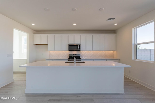 kitchen with stainless steel appliances, light hardwood / wood-style flooring, an island with sink, and white cabinets