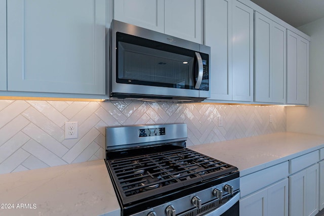 kitchen featuring white cabinetry, tasteful backsplash, stainless steel appliances, and light stone countertops