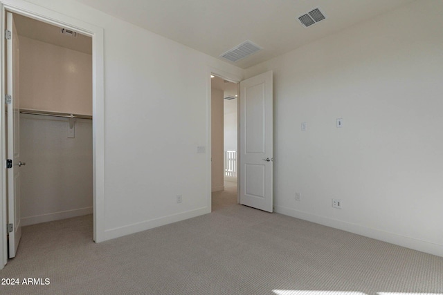 unfurnished bedroom featuring a closet, light colored carpet, and a walk in closet