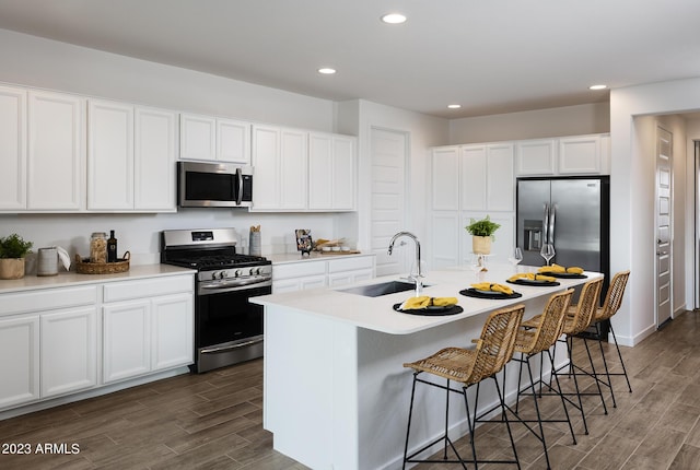 kitchen with dark wood-type flooring, sink, an island with sink, appliances with stainless steel finishes, and white cabinetry