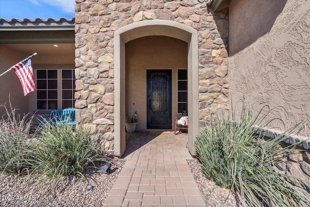 property entrance with a tiled roof, stone siding, and stucco siding