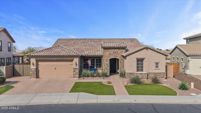 mediterranean / spanish home featuring decorative driveway, stone siding, fence, an attached garage, and a tiled roof