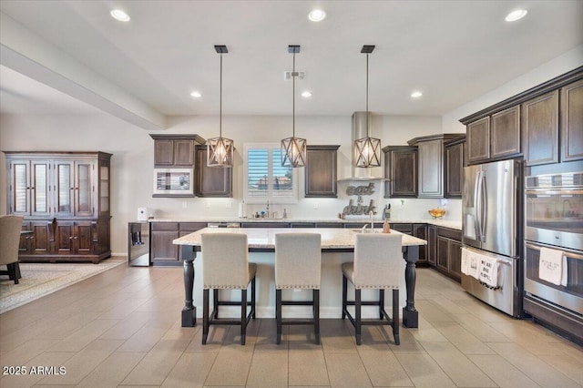 kitchen with dark brown cabinets, stainless steel appliances, a kitchen bar, and wall chimney range hood