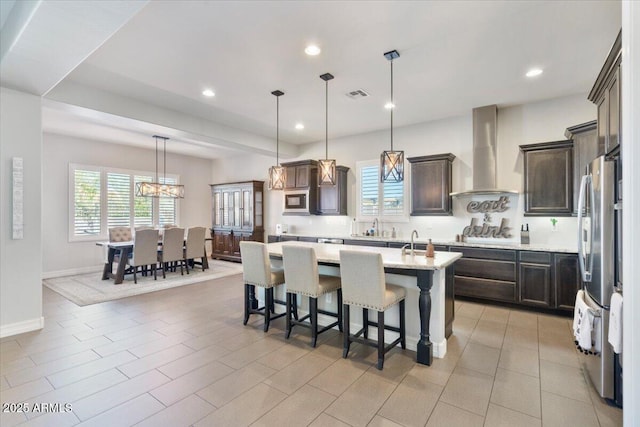 kitchen with visible vents, an island with sink, appliances with stainless steel finishes, wall chimney exhaust hood, and dark brown cabinets