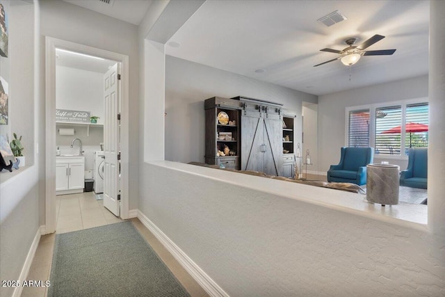 hallway with light tile patterned floors, baseboards, visible vents, washer / dryer, and a barn door