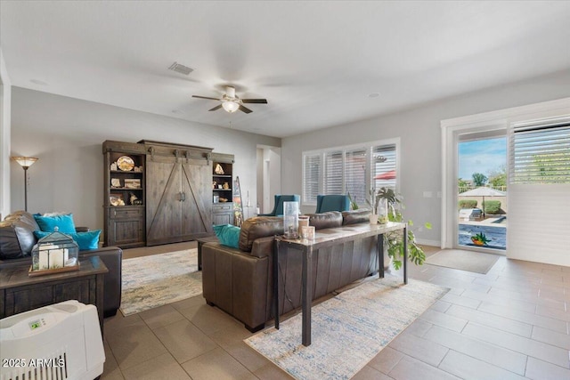 tiled living room featuring a barn door, baseboards, visible vents, and ceiling fan