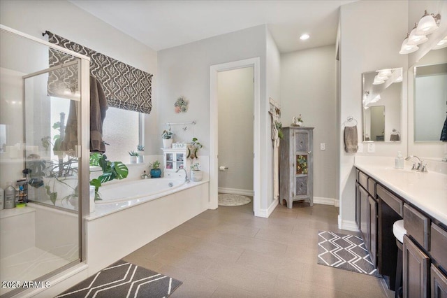 bathroom featuring baseboards, vanity, a garden tub, and a shower stall