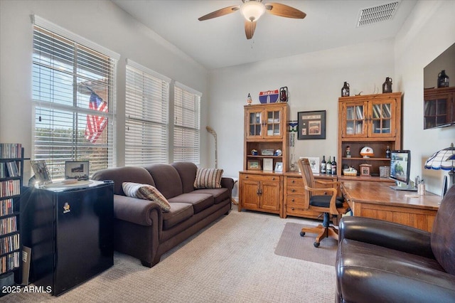 office space with light carpet, visible vents, and a ceiling fan