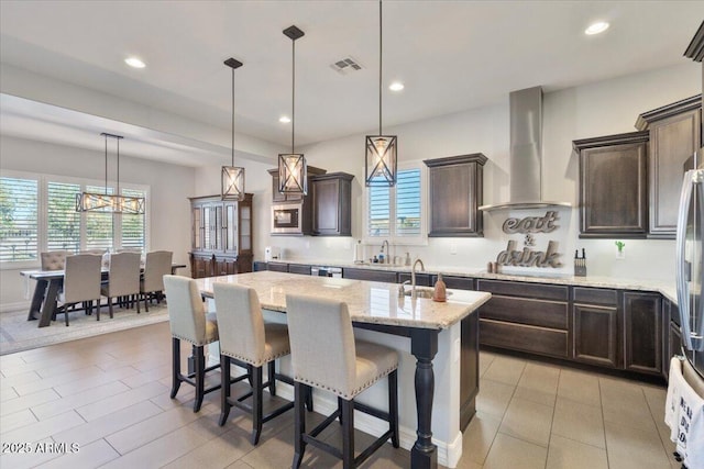 kitchen with visible vents, dark brown cabinetry, appliances with stainless steel finishes, wall chimney exhaust hood, and a sink