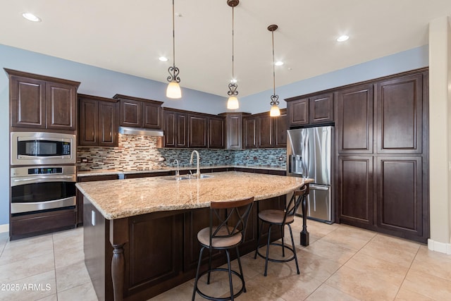 kitchen featuring sink, appliances with stainless steel finishes, dark brown cabinets, an island with sink, and decorative light fixtures