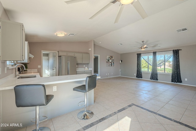 kitchen with lofted ceiling, a kitchen breakfast bar, sink, light tile patterned floors, and stainless steel refrigerator