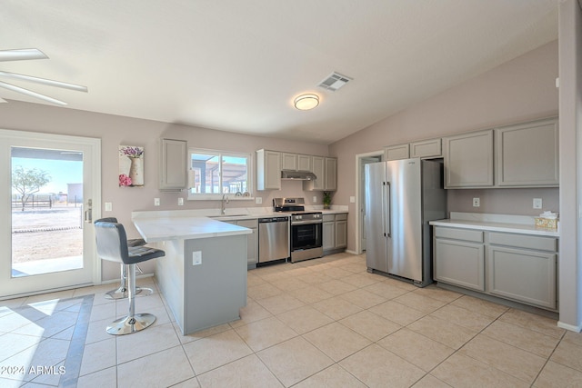 kitchen featuring kitchen peninsula, gray cabinetry, stainless steel appliances, vaulted ceiling, and a breakfast bar area