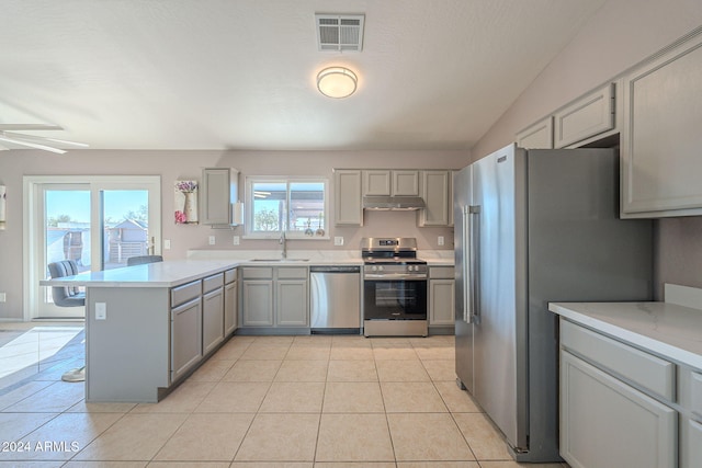 kitchen with stainless steel appliances, kitchen peninsula, vaulted ceiling, gray cabinets, and light tile patterned floors