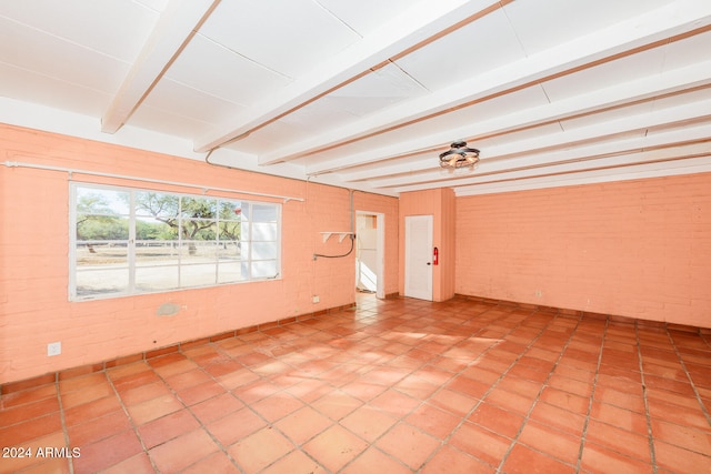 empty room with beam ceiling and brick wall