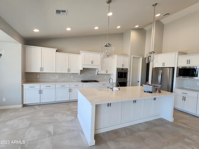 kitchen with appliances with stainless steel finishes, white cabinetry, backsplash, and an island with sink