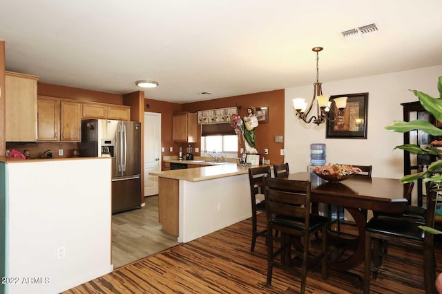 kitchen with a chandelier, stainless steel refrigerator with ice dispenser, hardwood / wood-style floors, decorative light fixtures, and kitchen peninsula