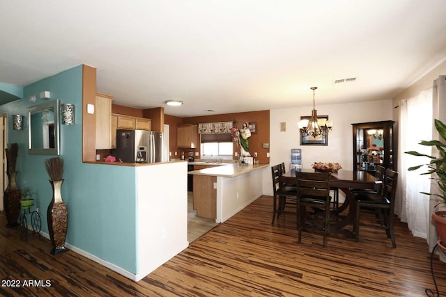 kitchen with a chandelier, stainless steel refrigerator with ice dispenser, hanging light fixtures, wood-type flooring, and kitchen peninsula