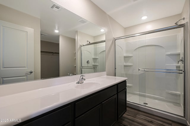 bathroom featuring wood finished floors, vanity, visible vents, a shower stall, and a walk in closet