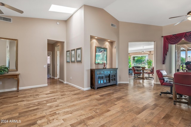 interior space featuring ceiling fan, a skylight, high vaulted ceiling, and light wood-type flooring