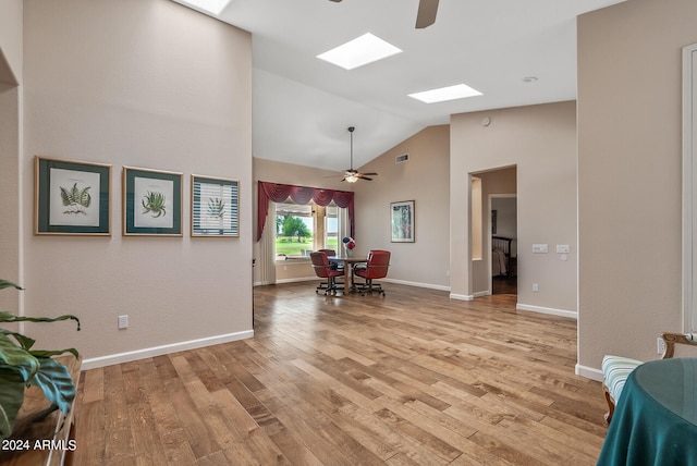 dining space featuring a skylight, high vaulted ceiling, ceiling fan, and light hardwood / wood-style flooring