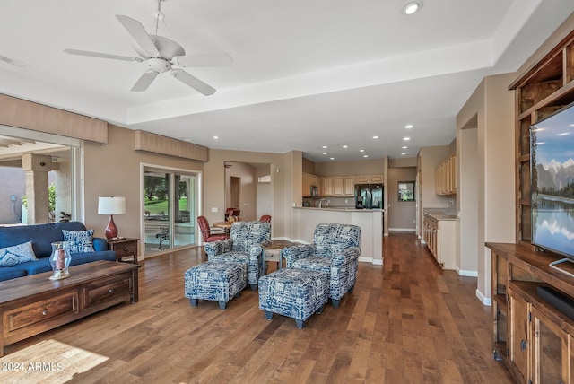 living room featuring ceiling fan, a raised ceiling, and light wood-type flooring