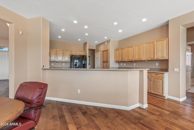 kitchen featuring dark hardwood / wood-style floors, black fridge, kitchen peninsula, light stone countertops, and light brown cabinets