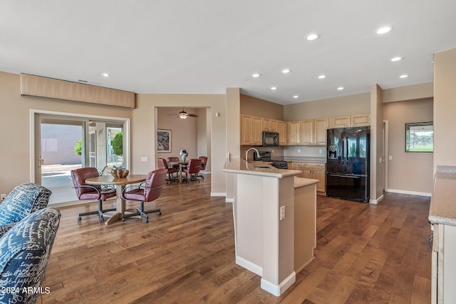 kitchen with dark wood-type flooring, light stone counters, black appliances, an island with sink, and light brown cabinets