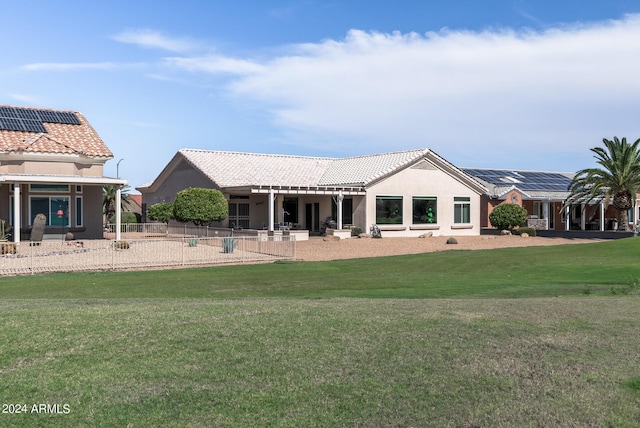 rear view of property featuring a lawn and solar panels