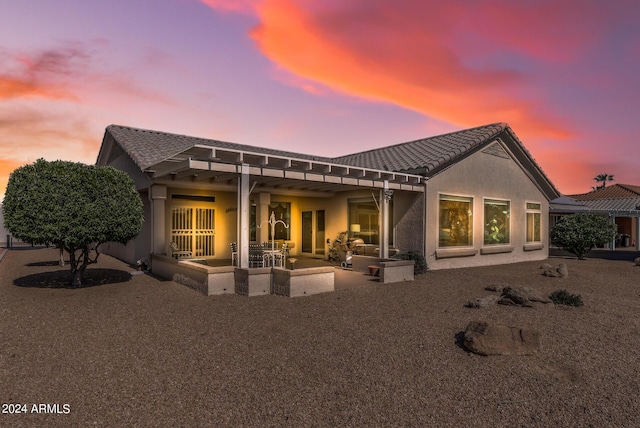 back house at dusk featuring a pergola and a patio area