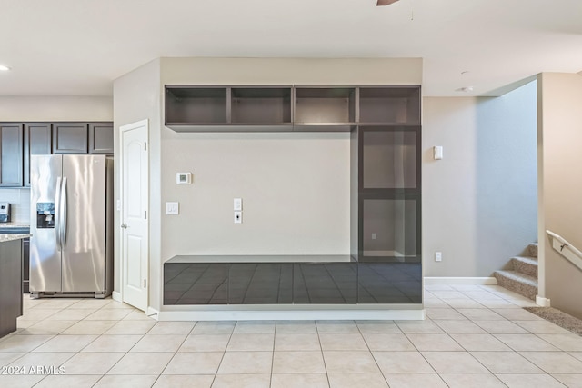 kitchen with backsplash, light stone counters, dark brown cabinetry, light tile patterned floors, and stainless steel fridge with ice dispenser