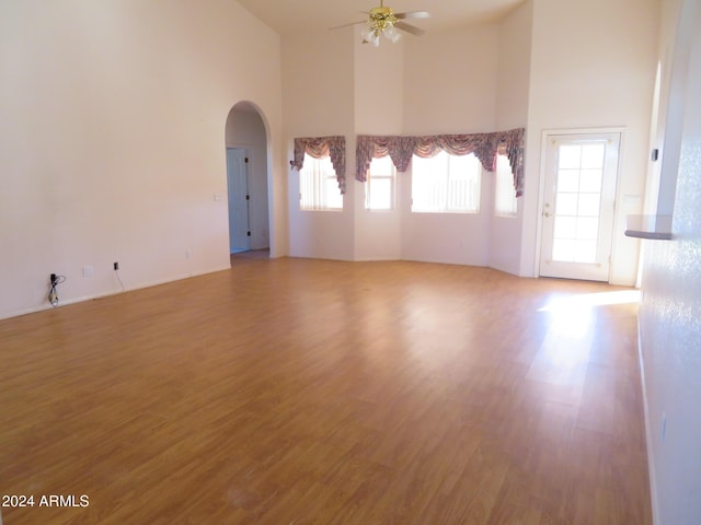 unfurnished room with ceiling fan, a wealth of natural light, a towering ceiling, and hardwood / wood-style flooring