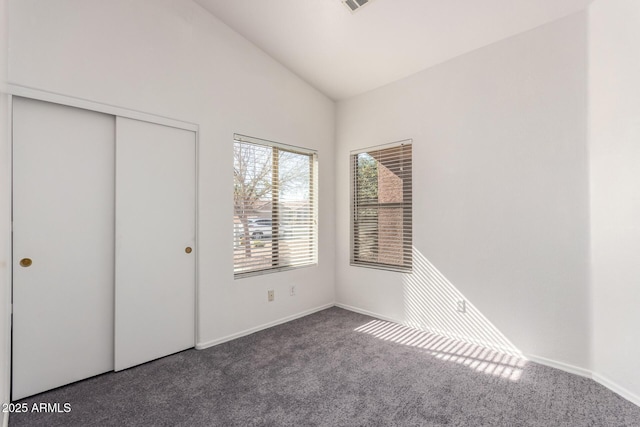 unfurnished bedroom with lofted ceiling, a closet, and dark colored carpet