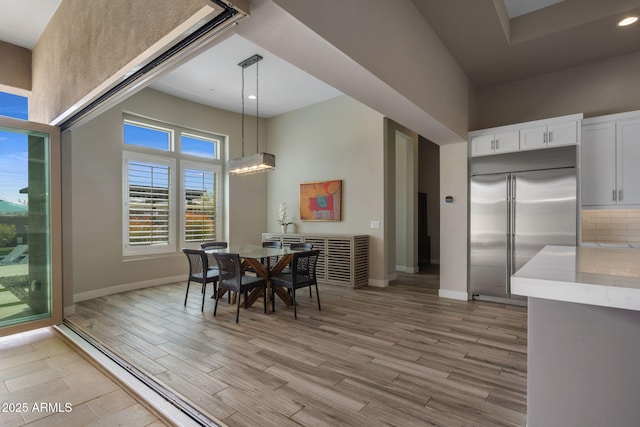 dining area featuring light wood finished floors, a notable chandelier, baseboards, and a towering ceiling