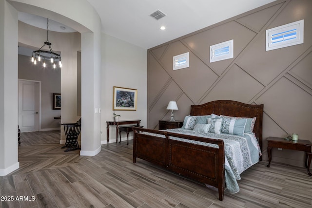 bedroom with visible vents, baseboards, wood finished floors, and a towering ceiling