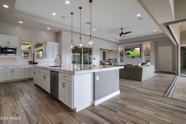 kitchen with wood tiled floor, a tray ceiling, a sink, white cabinets, and appliances with stainless steel finishes