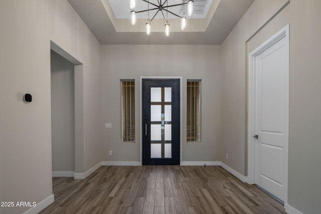 entryway with visible vents, a raised ceiling, wood finished floors, an inviting chandelier, and baseboards