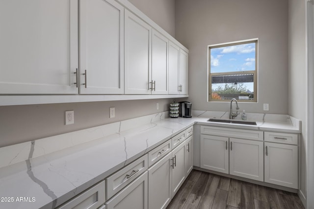 kitchen with white cabinets, light stone countertops, dark wood-style flooring, and a sink